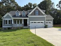Two-story home with a two car garage, gray paint and stone accents, situated on a lawn with surrounding trees at 78 Mineral Springs Way, Benson, NC 27504
