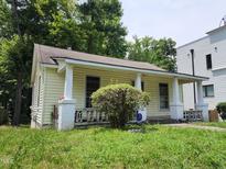 Charming yellow home featuring a covered porch, cozy front yard, and lush surrounding greenery at 1106 Fargo St, Durham, NC 27707