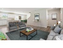 Bright open-concept living room featuring modern gray furniture, hardwood floors, and seamless flow to the kitchen at 16 Powder Ct, Angier, NC 27501