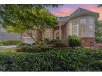 Beautiful two-story brick home featuring a lush landscaped front yard with mature trees and a garden bed at 109 Murdock Creek Ct, Cary, NC 27519