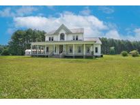 Expansive farmhouse with a charming wrap-around porch and lush green lawn on a sunny day at 1230 Sykes Rd, Spring Hope, NC 27882
