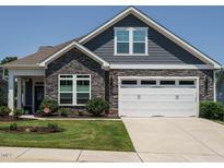 Charming home with stone accents, gray siding, well-manicured lawn, and a two-car white garage at 67 Blue Spruce Cir, Clayton, NC 27527