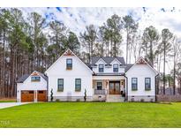 Charming white farmhouse-style home with a lush green lawn and three-car garage at 257 Rawhide Dr, Louisburg, NC 27549