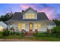 Charming home featuring a metal roof, inviting front porch, and beautiful landscaping at 6318 Hurdle Mills Rd, Roxboro, NC 27574