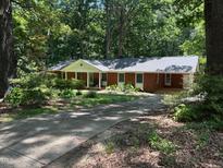 Charming red brick single story home with covered porch, set amongst a densely treed and landscaped front yard at 1225 Fairlane Rd, Cary, NC 27511