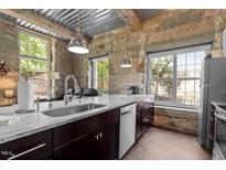 Modern kitchen featuring stone walls, stainless steel appliances, and granite countertops by bright windows at 1500 River Mill Dr # 101, Wake Forest, NC 27587