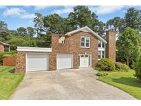 Inviting brick home featuring a spacious driveway leading to a two-car garage and lush landscaping at 6608 Quiet Cove Ct, Raleigh, NC 27612