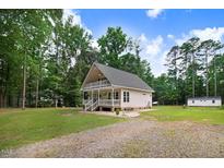 Charming home with inviting front porch, surrounded by lush greenery and a gravel driveway at 132 Ironwood Ln, Clayton, NC 27520