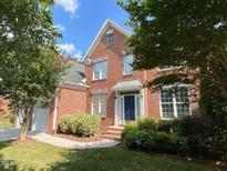 Traditional brick home with well-manicured lawn and blue front door, framed by mature trees under a sunny sky at 10108 Sporting Club Dr, Raleigh, NC 27617