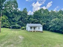 Quaint white home nestled on a grassy lawn with mature trees, complemented by a convenient metal carport at 229 Maple Dr, Oxford, NC 27565