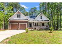Charming home featuring a covered front porch, two-car garage, and a well-manicured lawn surrounded by lush trees at 121 Quarterhorse Dr, Louisburg, NC 27549