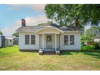Quaint one-story home featuring a covered front porch and a modest lawn under a partially cloudy sky at 402 Poplar St, Graham, NC 27253