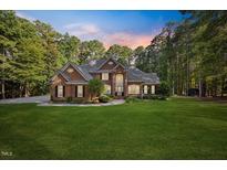 Charming two-story brick home with a lush green lawn and mature trees at sunset at 7529 Tynewind Dr, Wake Forest, NC 27587