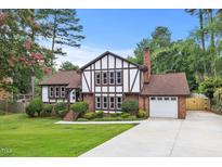 Charming Tudor-style home with brick and white facade, lush lawn, and a paved driveway leading to a garage at 2020 Port Royal Rd, Raleigh, NC 27609