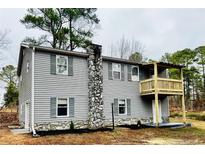 Charming two-story home with gray siding, stone chimney, and a cozy balcony overlooking the yard at 4454 Wire Rd, Linden, NC 28356