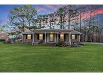 Charming brick home with a covered porch, manicured lawn, and a vibrant sunset backdrop at 1118 Cool Springs Rd, Sanford, NC 27330