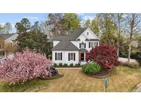 Charming two-story home featuring a landscaped front yard with flowering trees, black shutters, and a welcoming orange front door at 1300 Linden Ridge Dr, Holly Springs, NC 27540