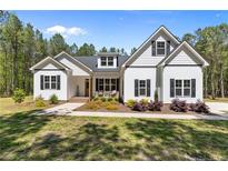 Charming two-story home features a symmetrical facade, lush landscaping, and a welcoming front porch with seating at 716 Wildlife Rd, Sanford, NC 27332