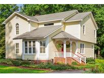 Charming two-story home with yellow siding, covered porch, brick steps, and mature landscaping at 1718 Carthage St, Sanford, NC 27330