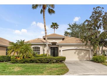 Tan one-story house with a two-car garage and lush landscaping at 9143 Willow Brook Dr, Sarasota, FL 34238