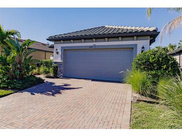 Single-story home with gray garage door, brick driveway, and landscaping at 2479 Brassica Dr, North Port, FL 34289