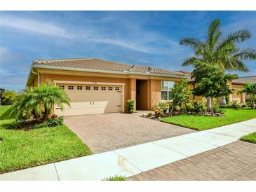 Tan house with beige garage door, landscaping, and paver driveway at 11786 Sistine Ln, Venice, FL 34293
