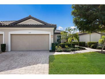 Tan three-car garage villa with paved driveway, landscaping, and walkway at 8199 Varenna Dr, Sarasota, FL 34231