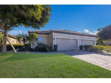 Tan two-car garage home with lush landscaping and a brick paver driveway at 8224 Varenna Dr, Sarasota, FL 34231