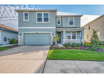 Two-story house with light teal siding, stone accents, and a two-car garage at 5755 Woodland Sage Dr, Sarasota, FL 34238