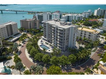 Stunning aerial view of a modern condo building with a pool, lush landscaping, and picturesque waterfront backdrop at 325 Golden Gate Pt # 802, Sarasota, FL 34236