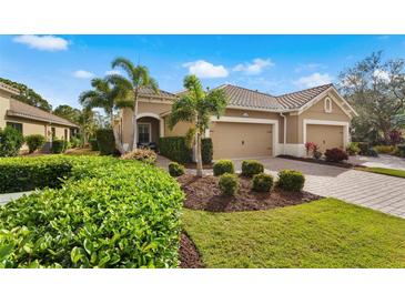 Tan two-car garage home with lush landscaping and a brick driveway at 12199 Sebring Ln, Venice, FL 34293