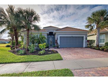 Single-story home with gray garage door, brick paver driveway, and lush landscaping at 19451 Quisto St, Venice, FL 34293