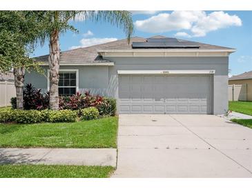 One-story home with gray siding, solar panels, and a two-car garage. Lush landscaping with palm trees and manicured lawn at 208 Cascade Bend Dr, Ruskin, FL 33570