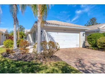 Single-story home with white garage door and paved driveway, landscaping, and palm trees at 7613 Camminare Dr, Sarasota, FL 34238