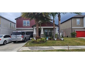 Two-story red house with landscaping, driveway, and two parked cars at 12315 Ballentrae Forest Dr, Riverview, FL 33579