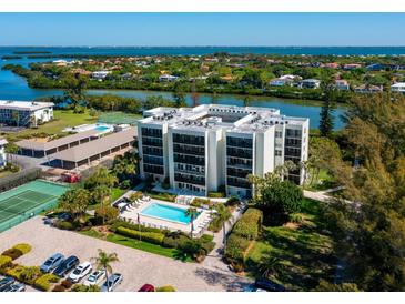 Aerial view of waterfront condo building with pool, tennis court, and parking at 3240 Gulf Of Mexico Dr # B104, Longboat Key, FL 34228