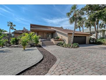 Inviting exterior featuring a tile roof, palm trees, beautiful landscaping, brick driveway, and attached garage at 3131 Bayou Sound, Longboat Key, FL 34228
