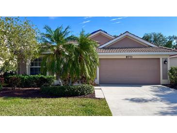 Beige house with two-car garage, landscaping, and palm trees at 8773 Stone Harbour Loop, Bradenton, FL 34212