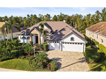 Beautiful home exterior with a well-manicured lawn, lush landscaping, and a paver driveway leading to a three-car garage at 6815 Turnberry Isle Ct, Lakewood Ranch, FL 34202