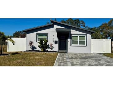 Modern single story home with gray exterior, paver driveway, and white fence at 4029 9Th S Ave, St Petersburg, FL 33711