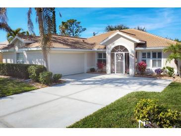 Tan house with white trim, two-car garage, and landscaped yard at 8240 Parkside Dr, Englewood, FL 34224