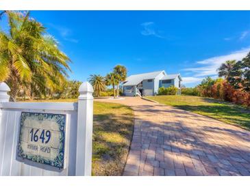 Light blue house with metal roof, paver driveway, and tropical landscaping at 1649 Manor Rd, Englewood, FL 34223