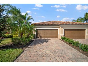 Two-car garage with paver driveway, lush landscaping, and Spanish-style tile roof at 114 Babbling Brook Run, Bradenton, FL 34212