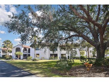 Beautiful condo building featuring well maintained grounds, mature trees and landscaping under a partly cloudy blue sky at 796 Capri Isles Blvd # 242, Venice, FL 34292