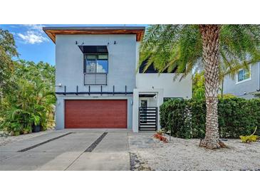 Contemporary two-story home featuring a modern facade, wood garage door, and tropical landscaping at 2434 Wood St, Sarasota, FL 34237