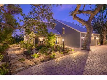 Gray house with a metal roof, landscaped yard, and brick paver driveway at 716 Tropical Cir, Sarasota, FL 34242