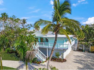 Beautiful light blue Key West home featuring a well-manicured lawn, lush tropical foliage, and a brick driveway at 3445 Anglin Dr, Sarasota, FL 34242