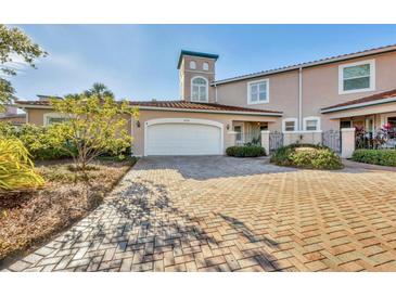 Tan two-story townhome with white garage door, brick driveway, and lush landscaping at 1719 Starling Dr # 1719, Sarasota, FL 34231