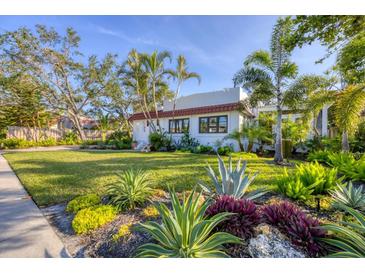 Beautifully landscaped front yard featuring tropical plants and a well-maintained lawn with a white house and red tile roof at 1864 Clematis St, Sarasota, FL 34239