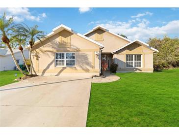 Tan house with a green lawn, palm trees, and a driveway at 21264 Wynyard Ave, Port Charlotte, FL 33954